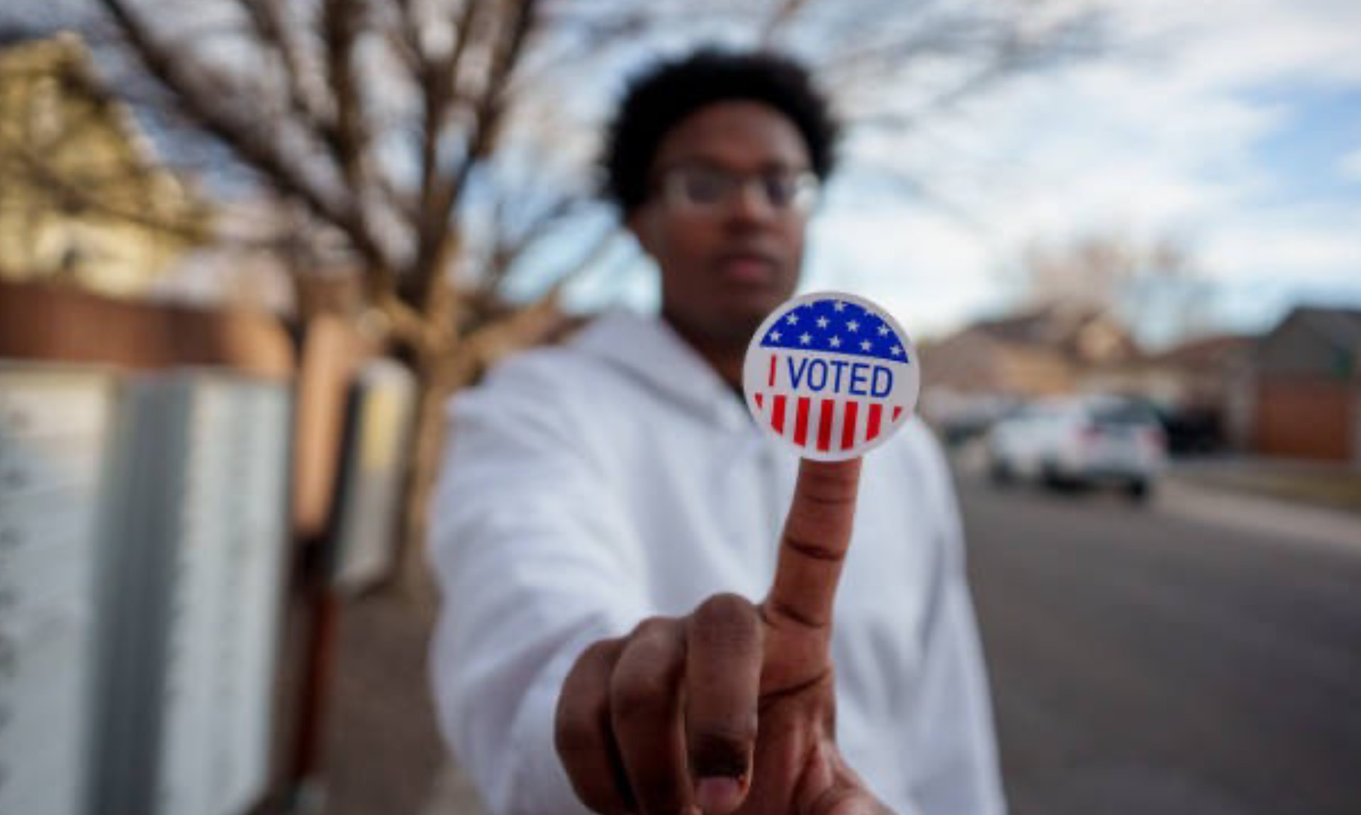 Young African American Man in His Twenties Holding an I Voted Sticker Up to the Camera and Smiling