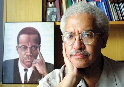 Manning Marable seated beside a portrait of Malcolm X, representing Black Studies scholarship and institution building at Columbia University.