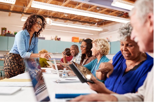 A congregational leader helps older adults use laptops and tablets during a community program.